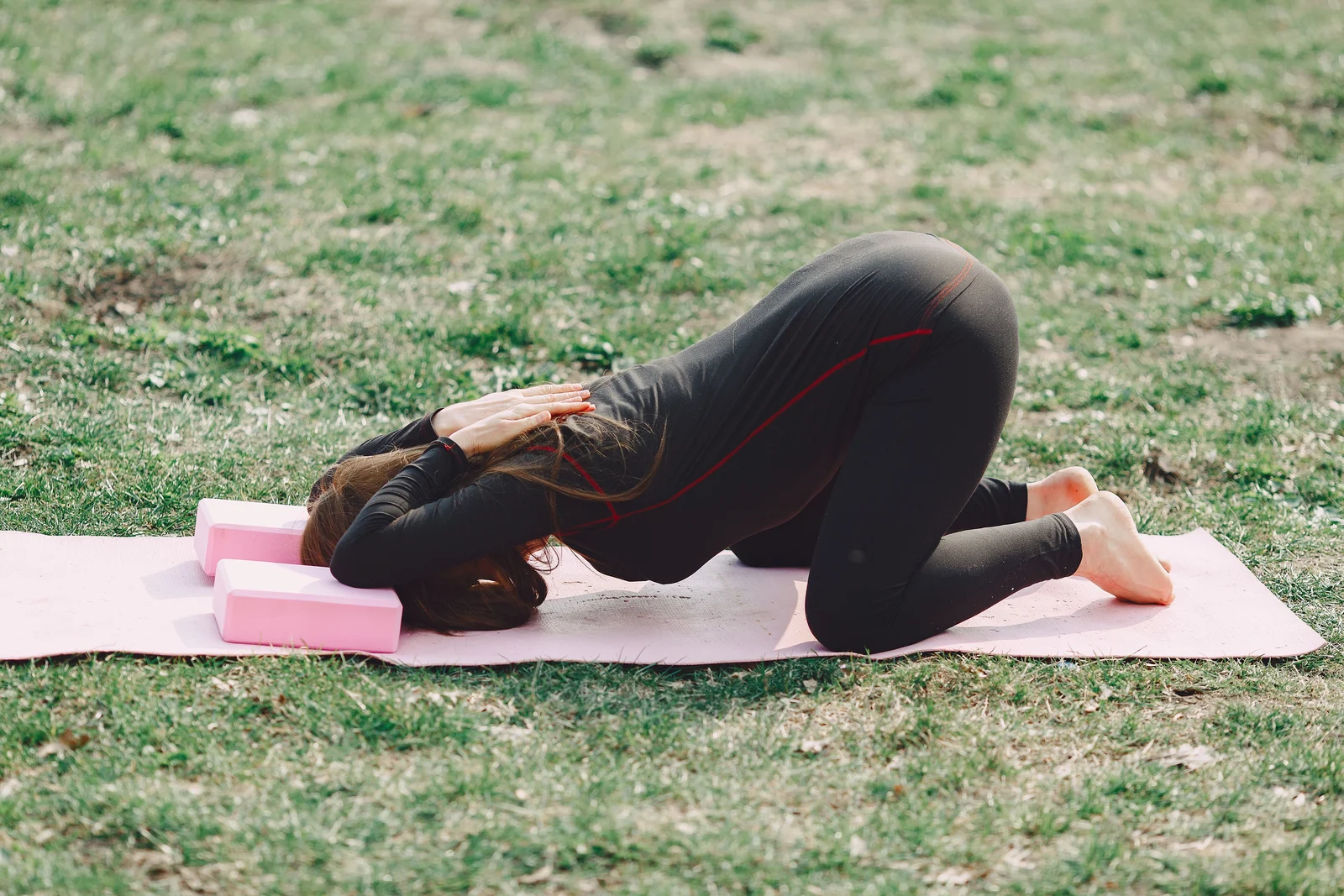 A woman folding forward with her forearms resting on yoga blocks on a mat, the blocks bringing the floor up to her.